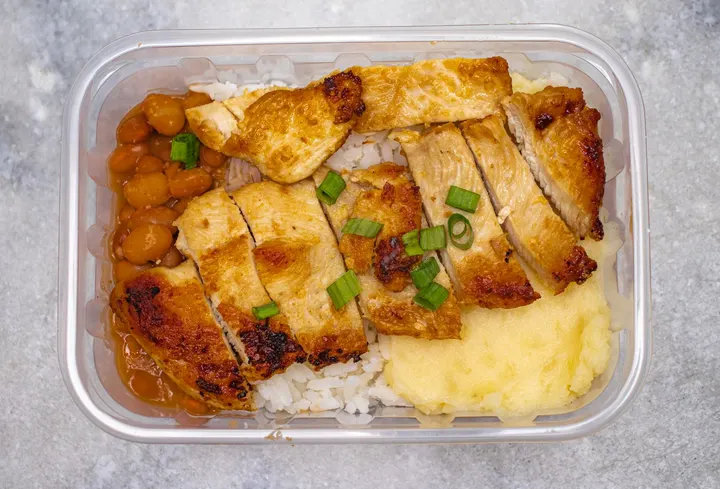 Grilled chicken with rice, beans and mashed potatoes in a container